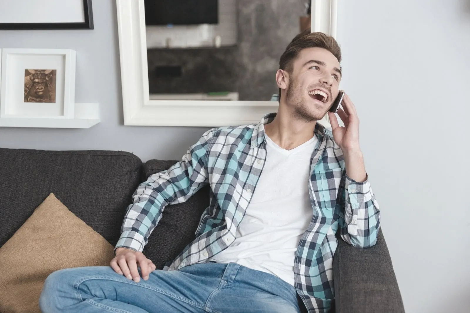 laughing man sitting in the couch inside living room talking by phone and looking away