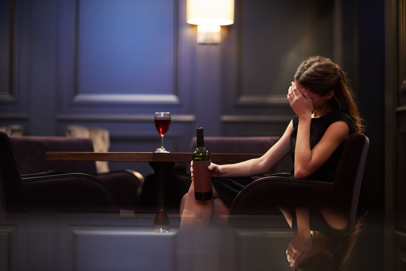 jovem mulher solitária e triste com uma garrafa de vinho tinto num hotel de luxo