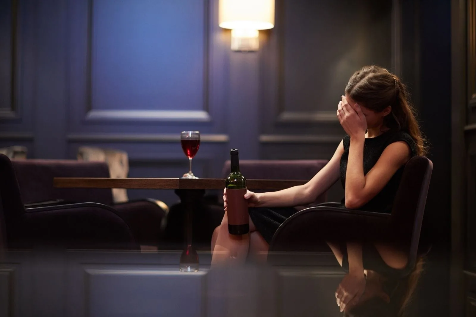 lonely young woman sad with a bottle of red wine in a luxurious hotel
