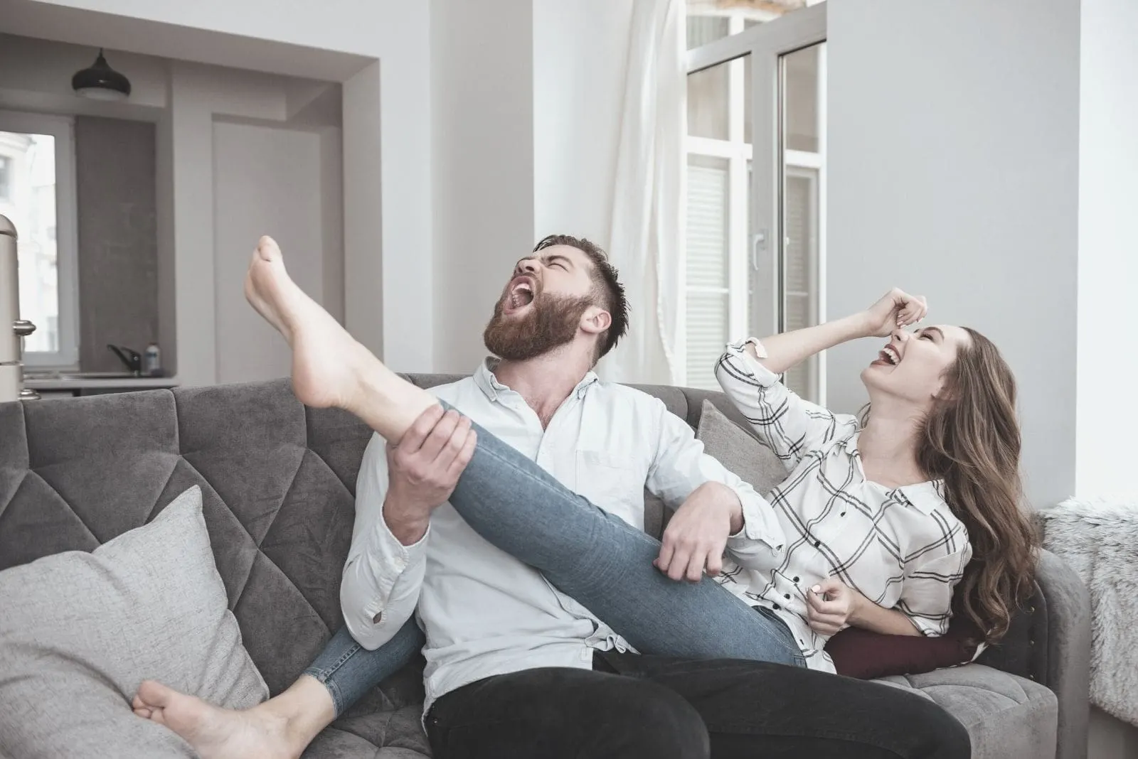 lovely funny couple sitting in sofa with the man imagining the woman's leg is a guitar