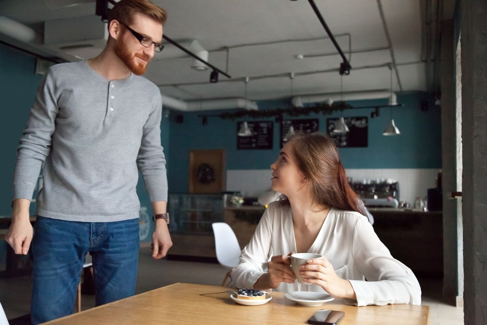 hombre acercandose a una mujer en el cafe tomando su comida