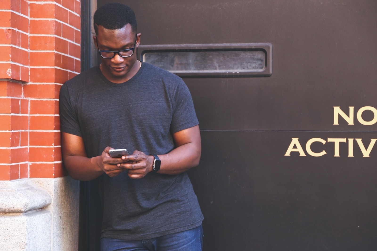 man leaning on brick wall while using smartphone