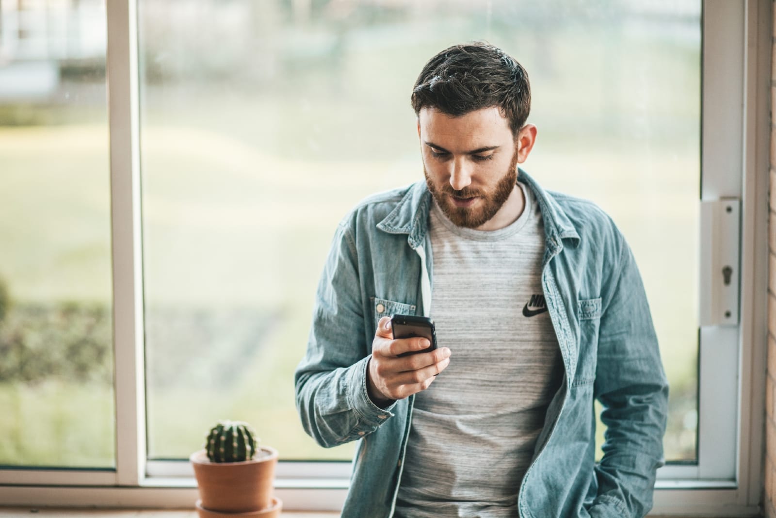 man looking at phone while standing near window
