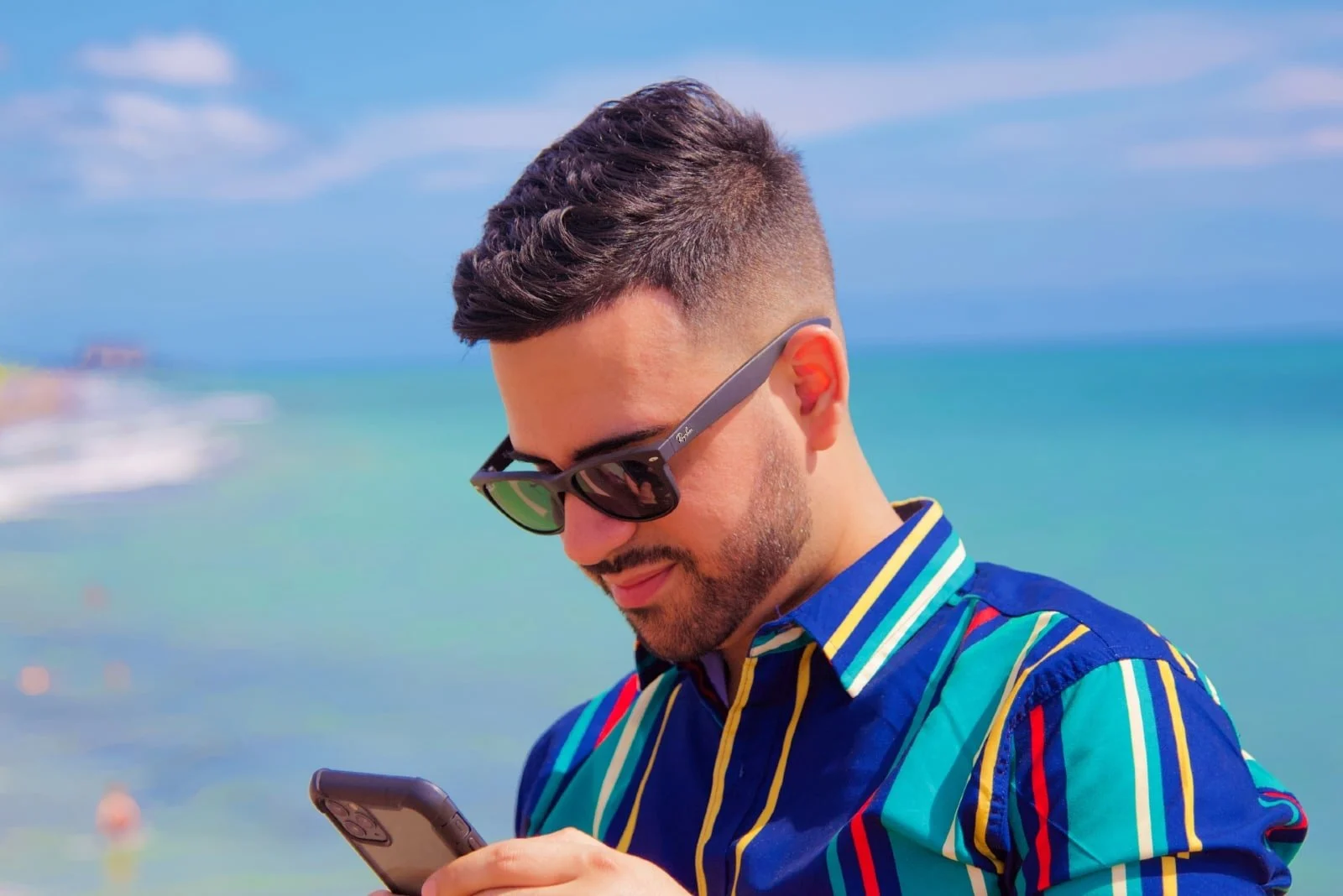 man looking at phone while standing near sea