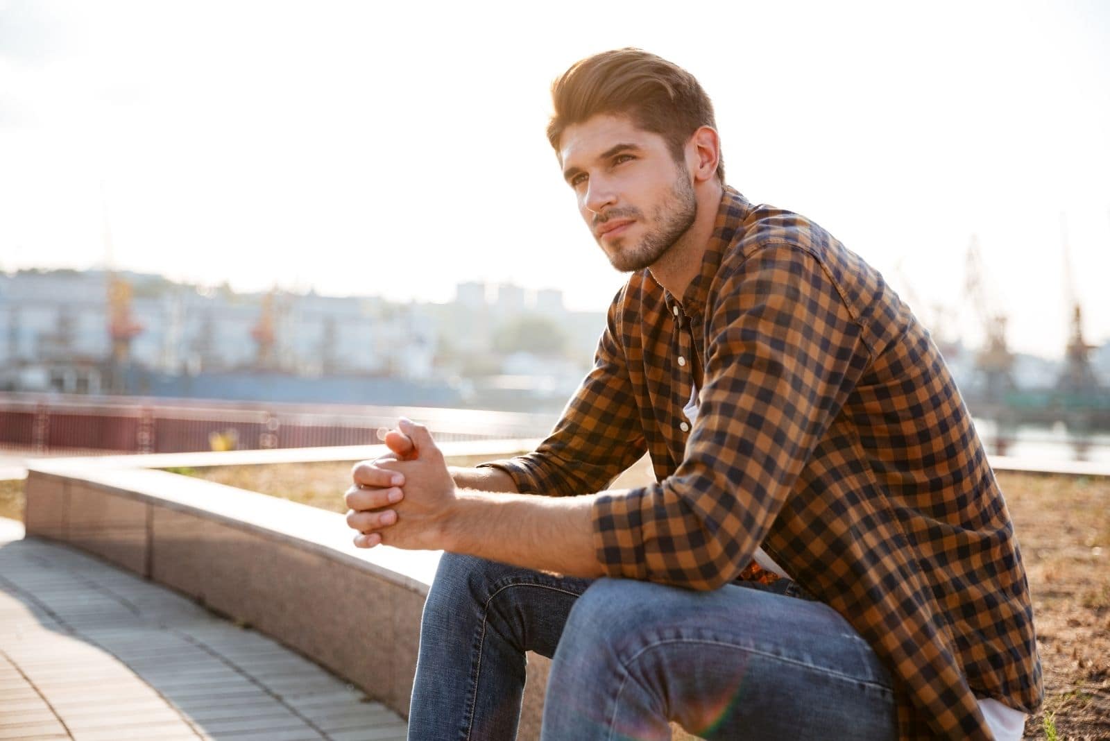 man sitting in the sidewalk in a concrete planter in the park thinking deeply