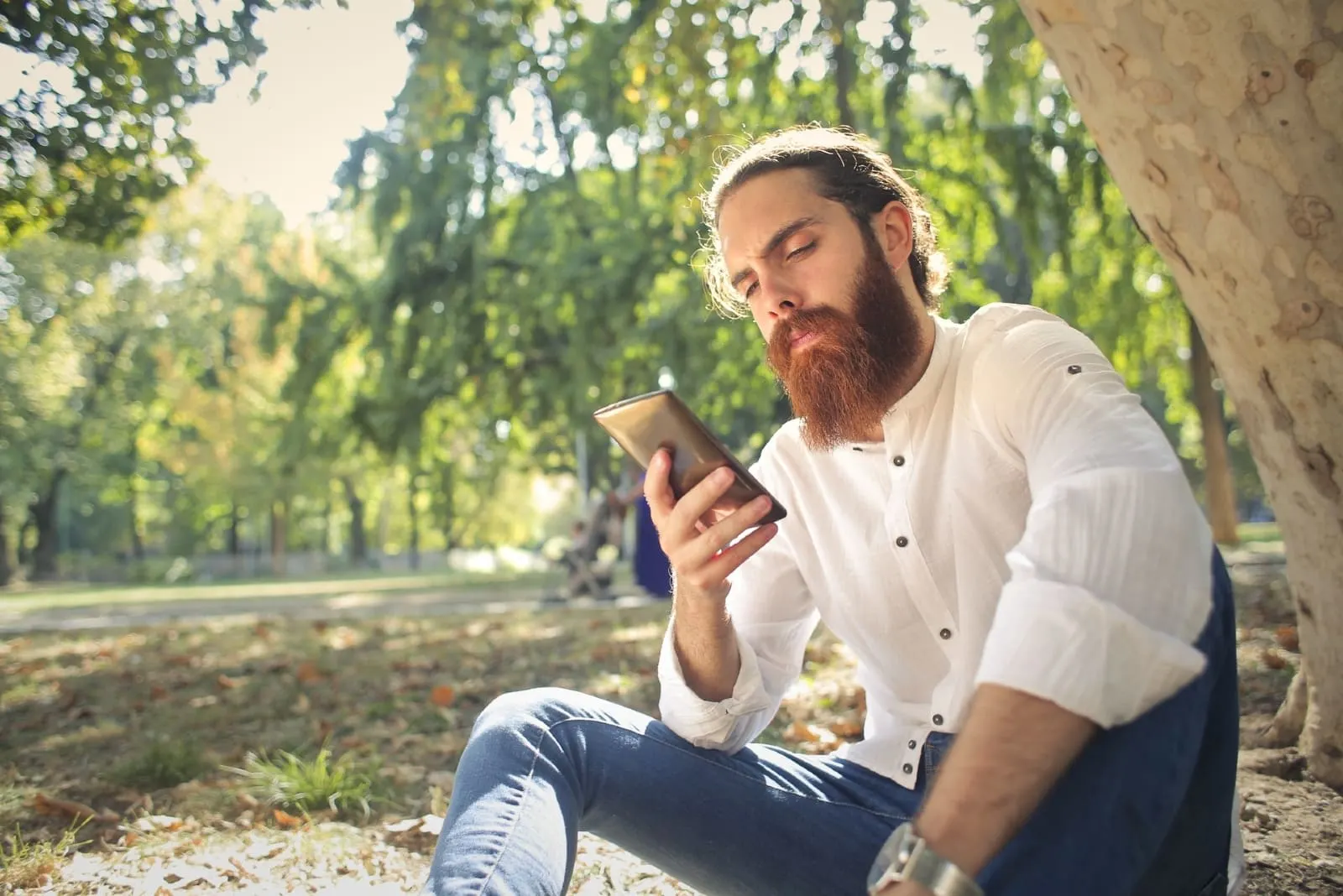man looking at phone while sitting near tree