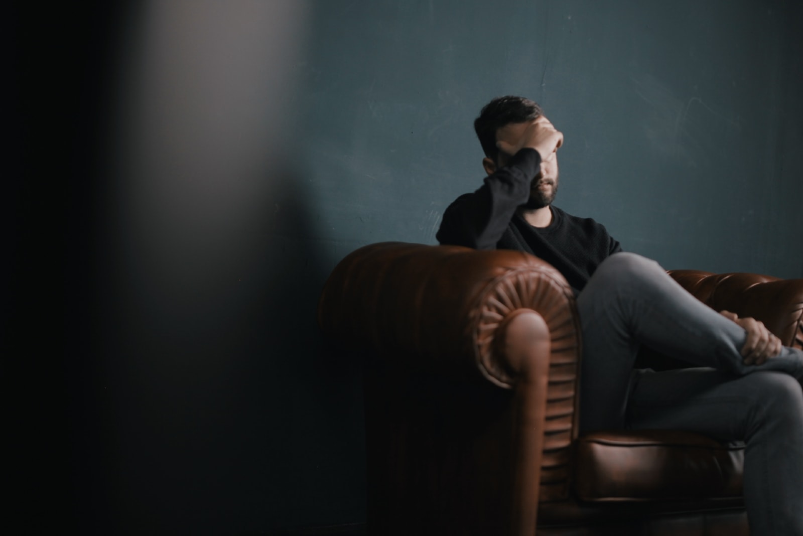 homem triste de camisola preta sentado num cadeirão