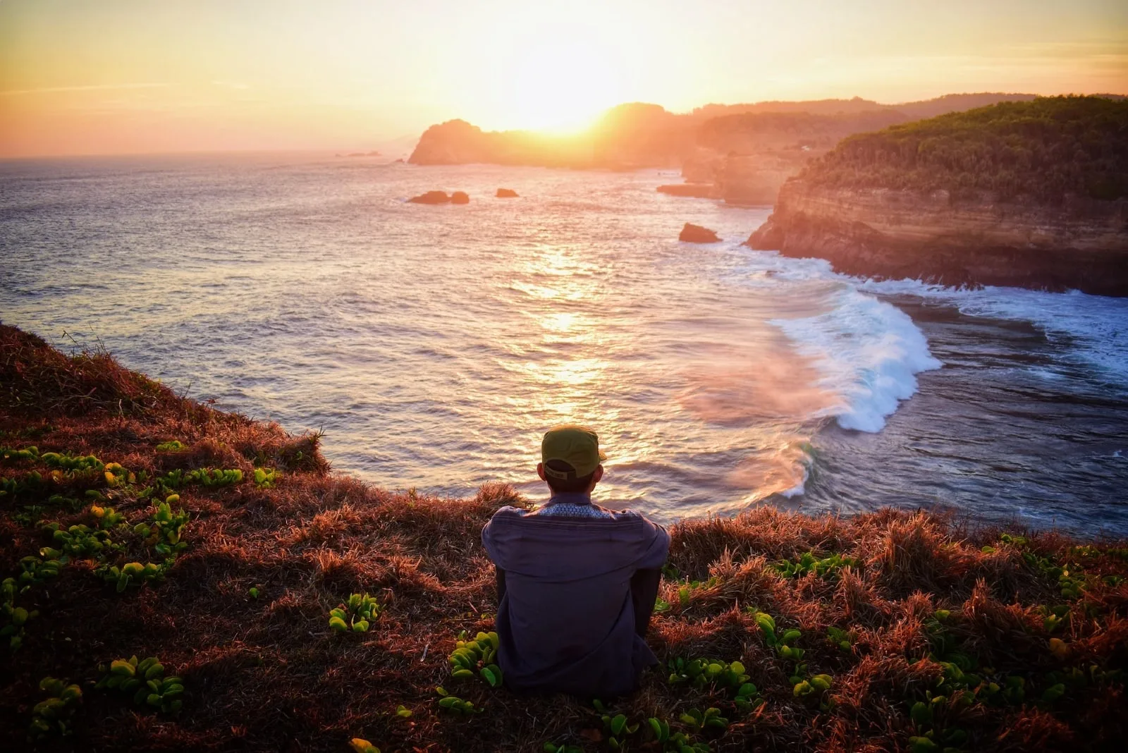 man sitting on grass looking at ocean
