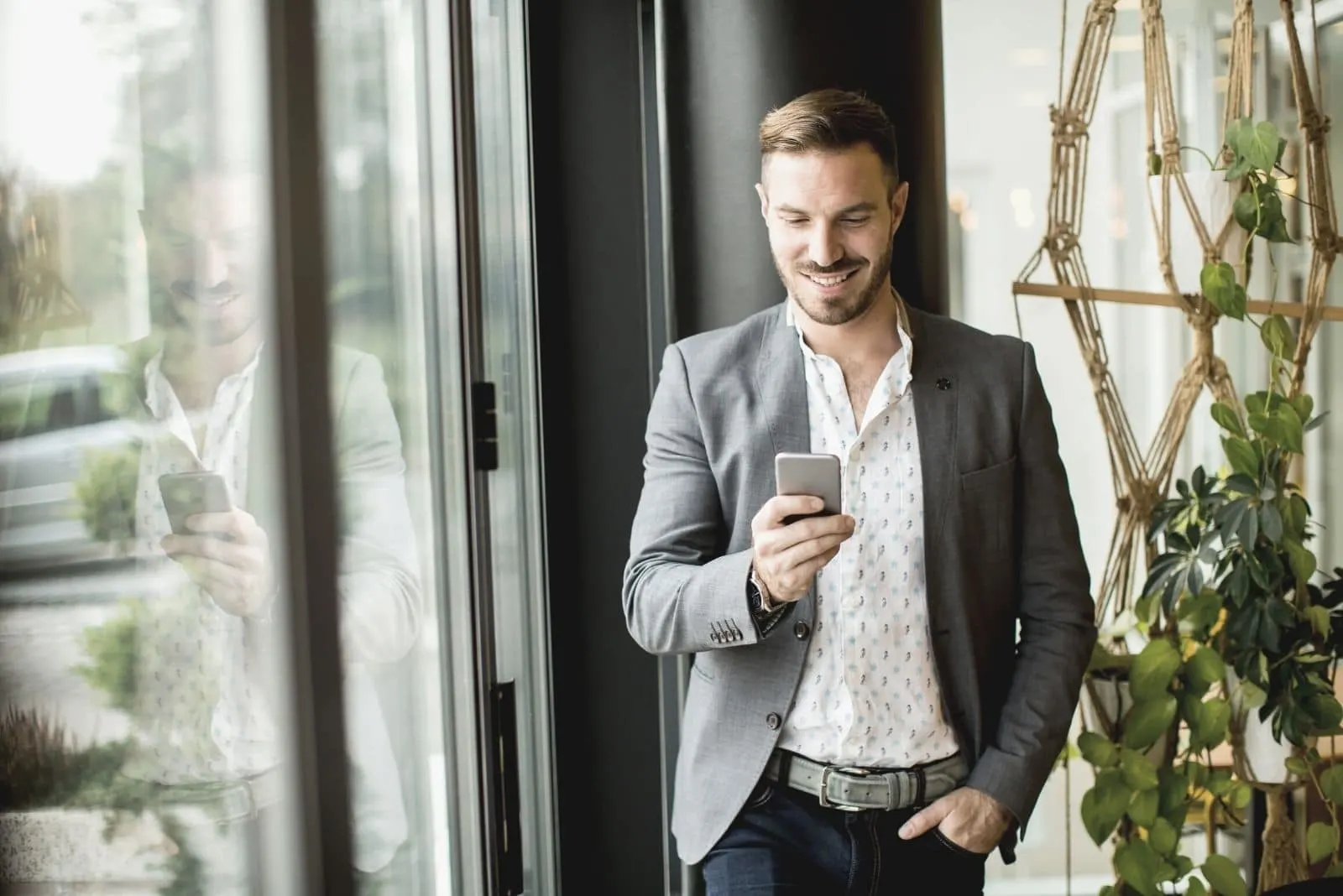man standing inside the office smiling and looking at his phone with one hand on his pocket