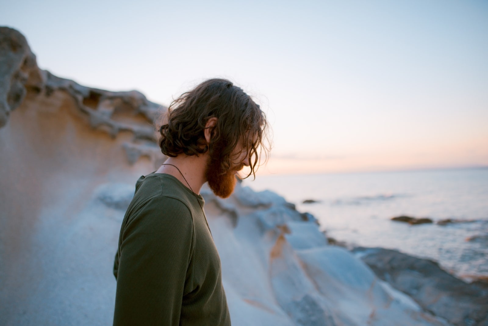 sad man in green shirt standing near sea