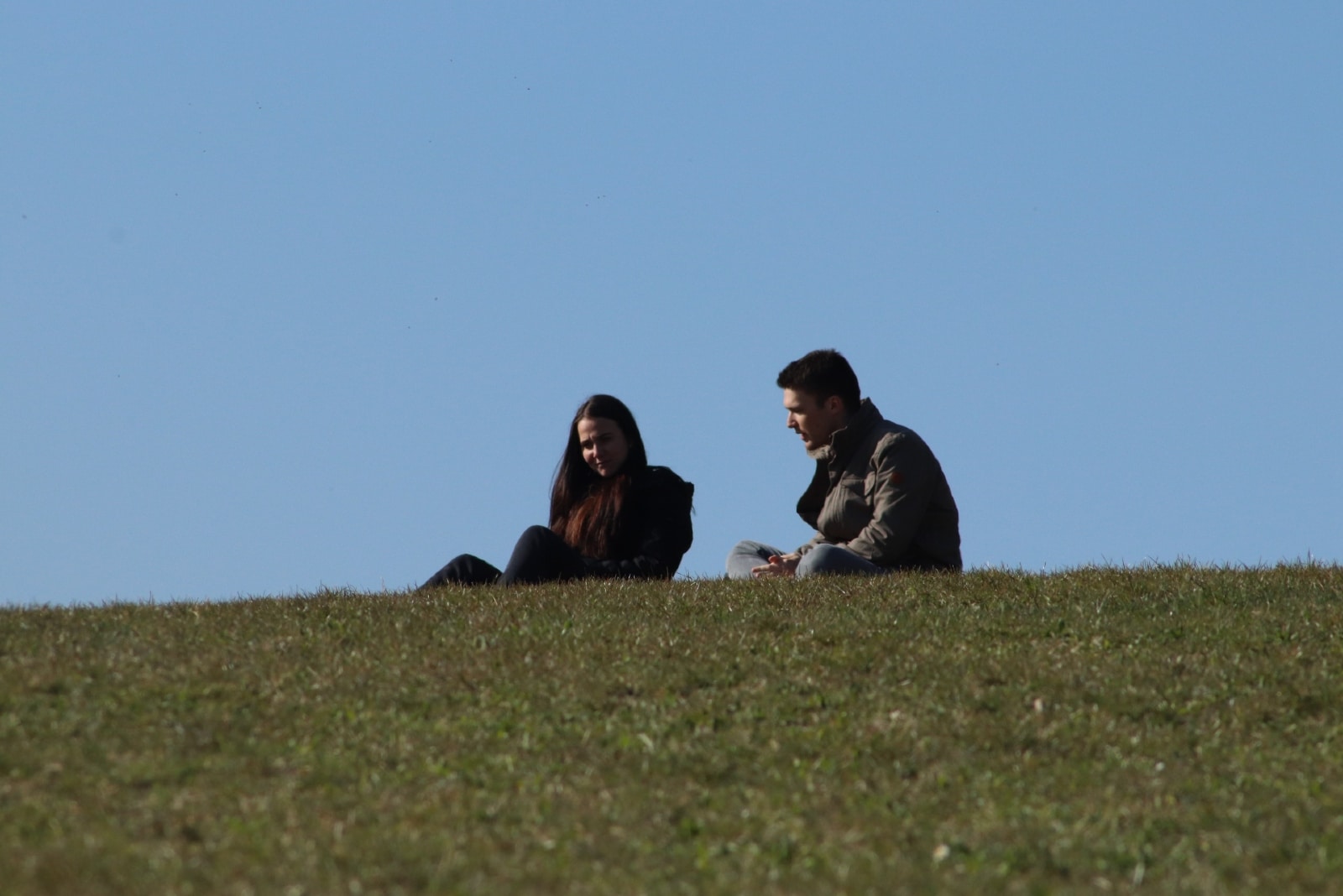 man talking to woman while sitting on grass