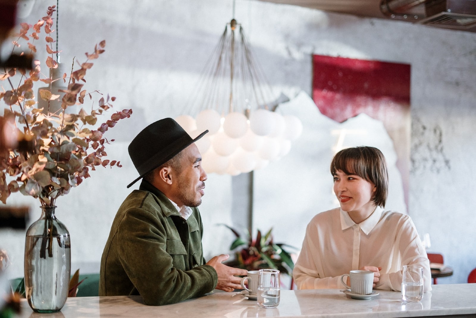 man in green jacket talking to woman in cafe