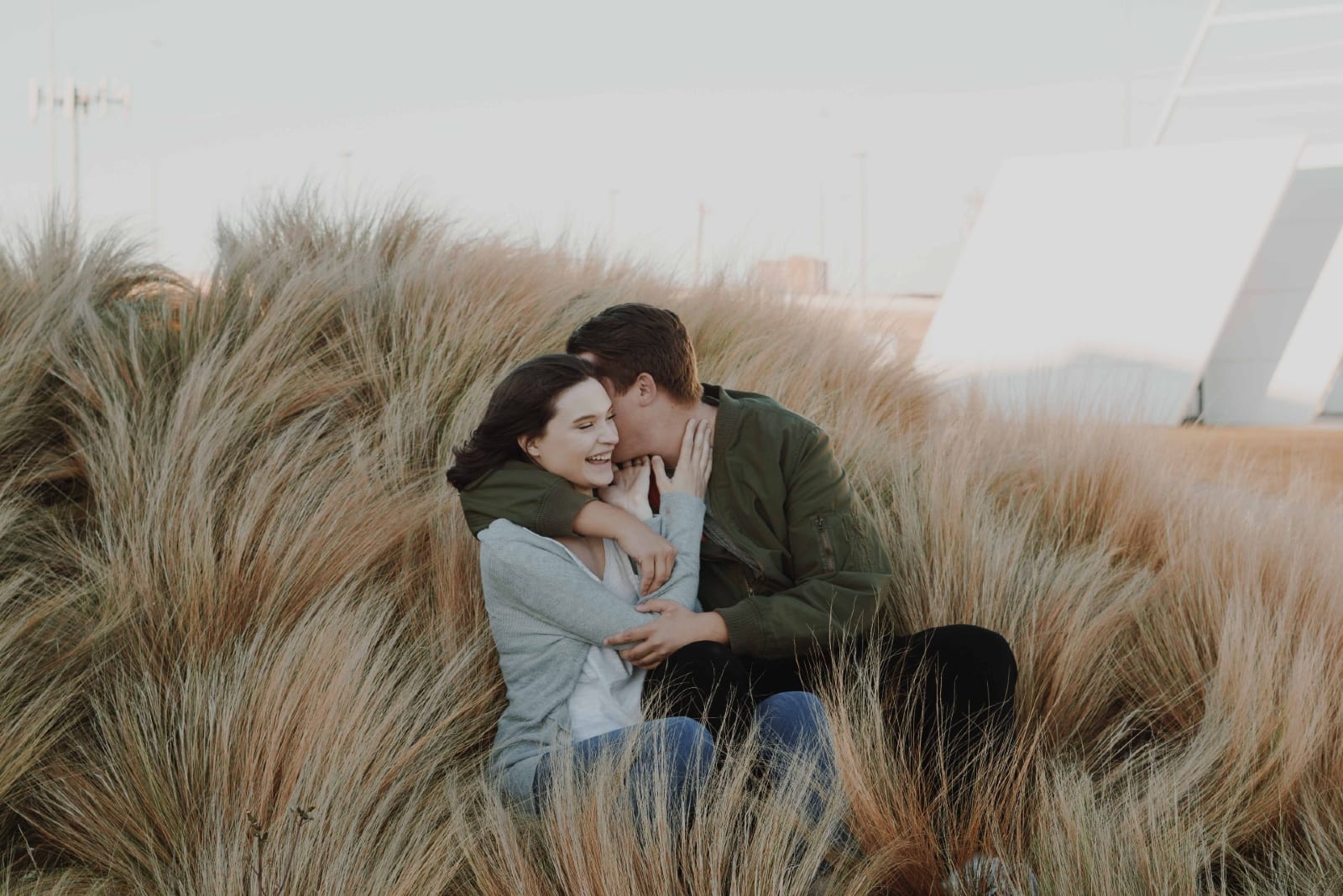 man whispering in woman's ear while sitting on brown grass