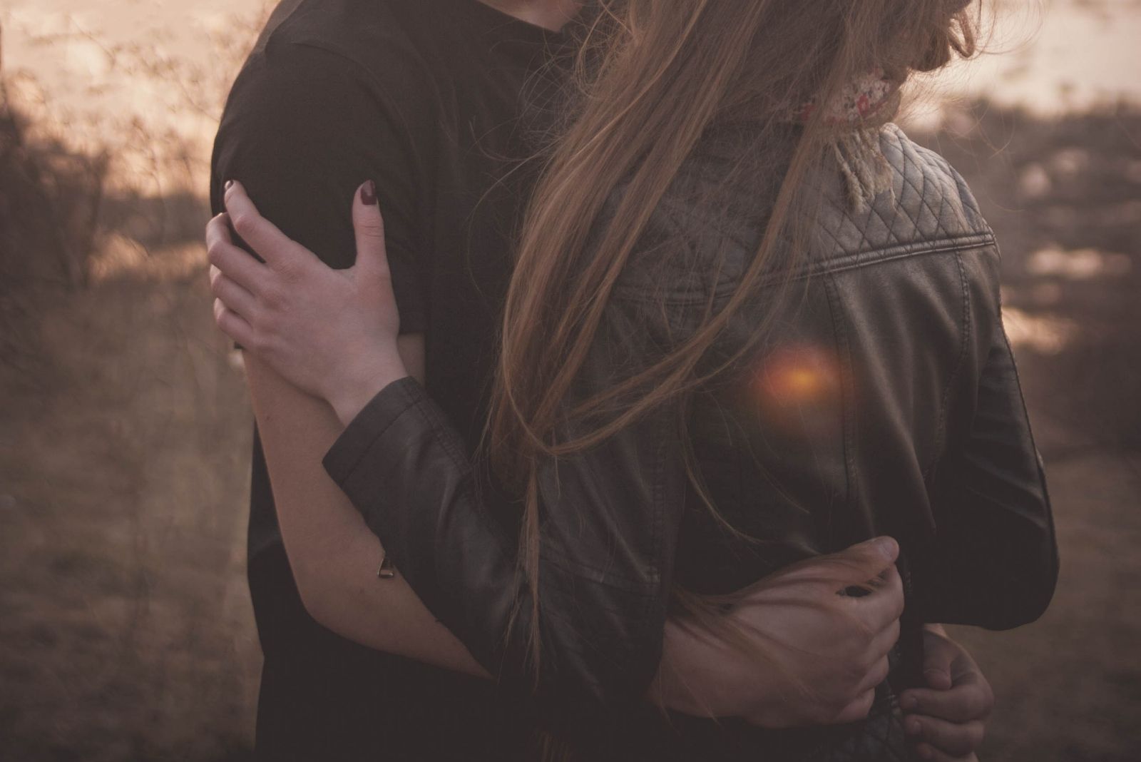 man's hand around the woman's waist while kissing outdoors in cropped image