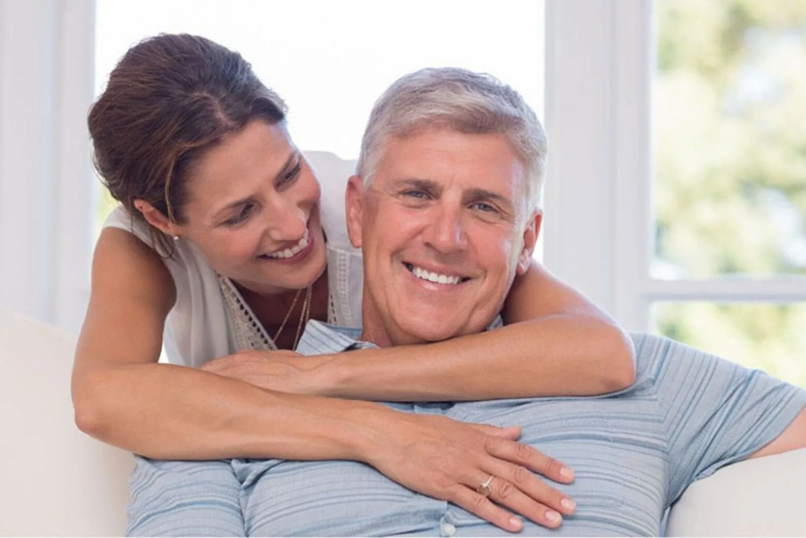 mature man sitting hugged by a younger woman inside the living room