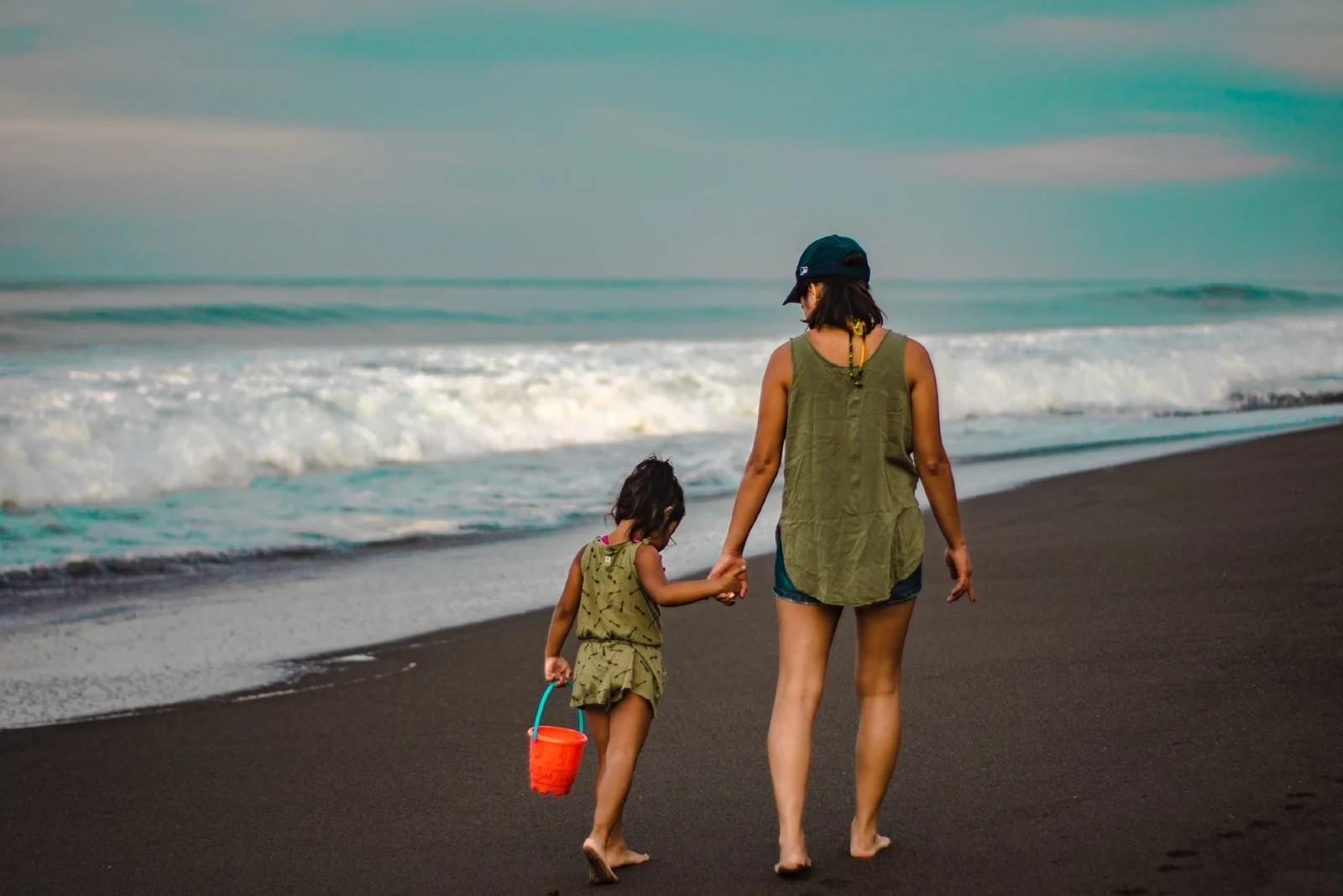 mother and daughter holding hands while walking on shore