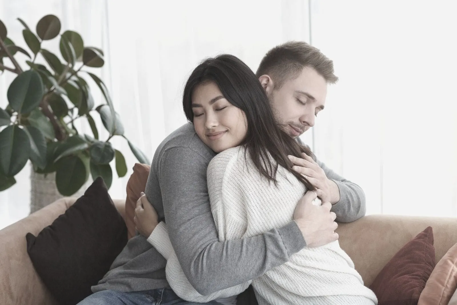 multicultural couple hugging and sitting in the sofa inside living room