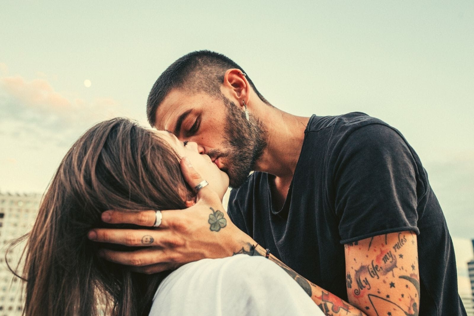 una giovane coppia felice che si bacia appassionatamente all'aperto con le braccia del ragazzo sul viso della donna