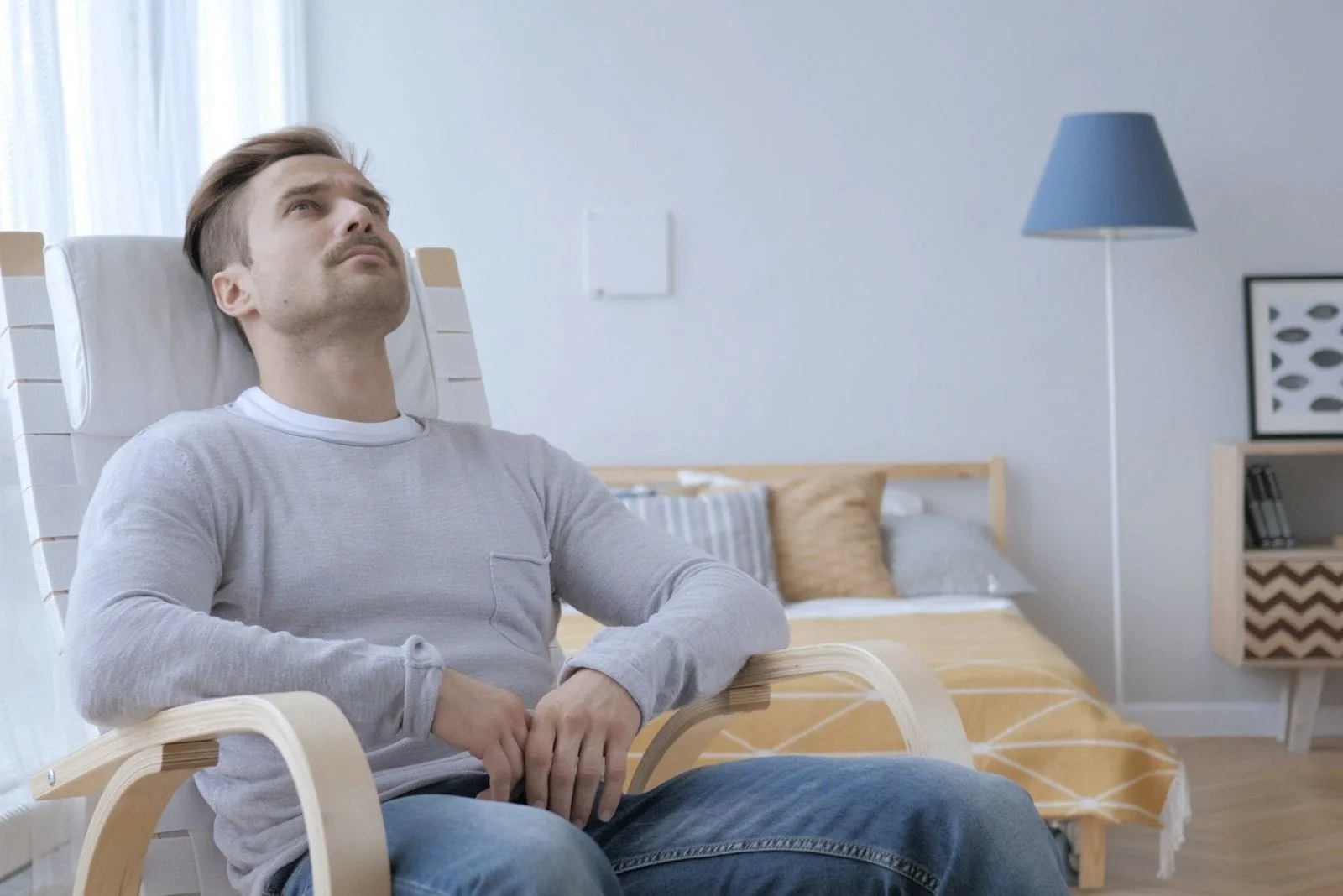pensive adult man sitting on the chair inside the bedroom looking at the roof