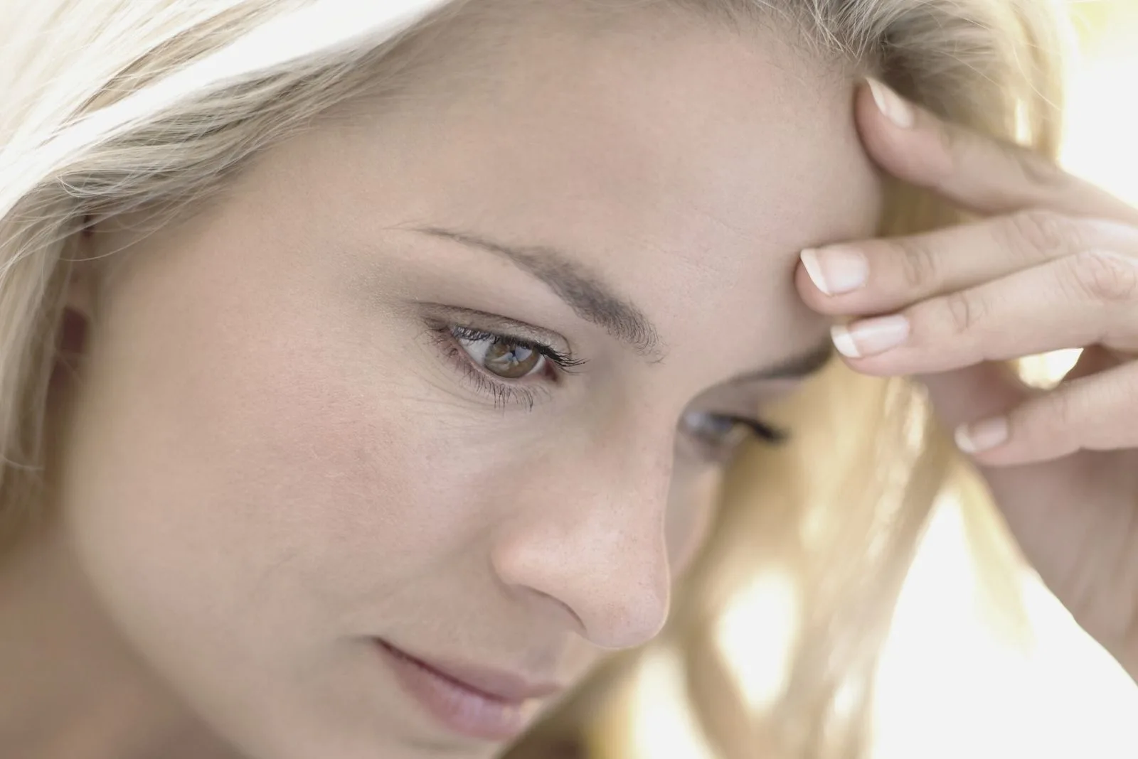 pensive blonde woman looking down and holding her head focus on her face
