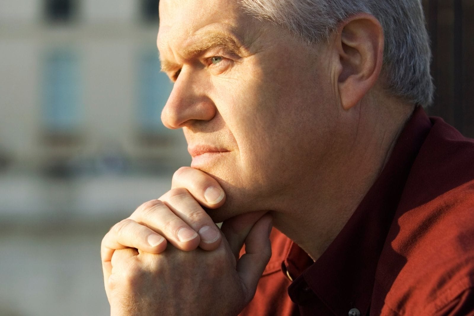 pensive mature man sitting outdoors with hands on his chin