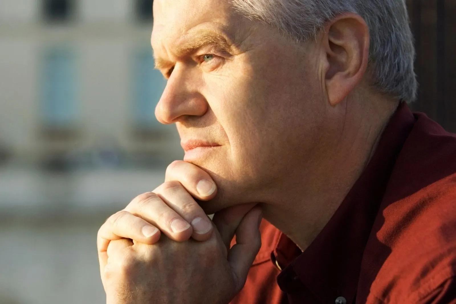 pensive mature man sitting outdoors with hands on his chin