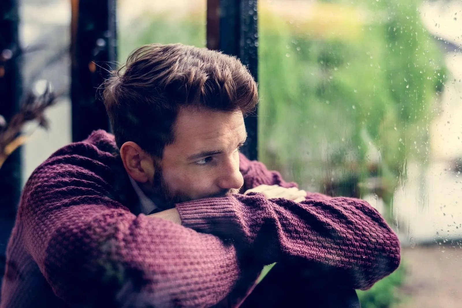 pensive middle age man sitting beside the window looking outside and leaning on his arms