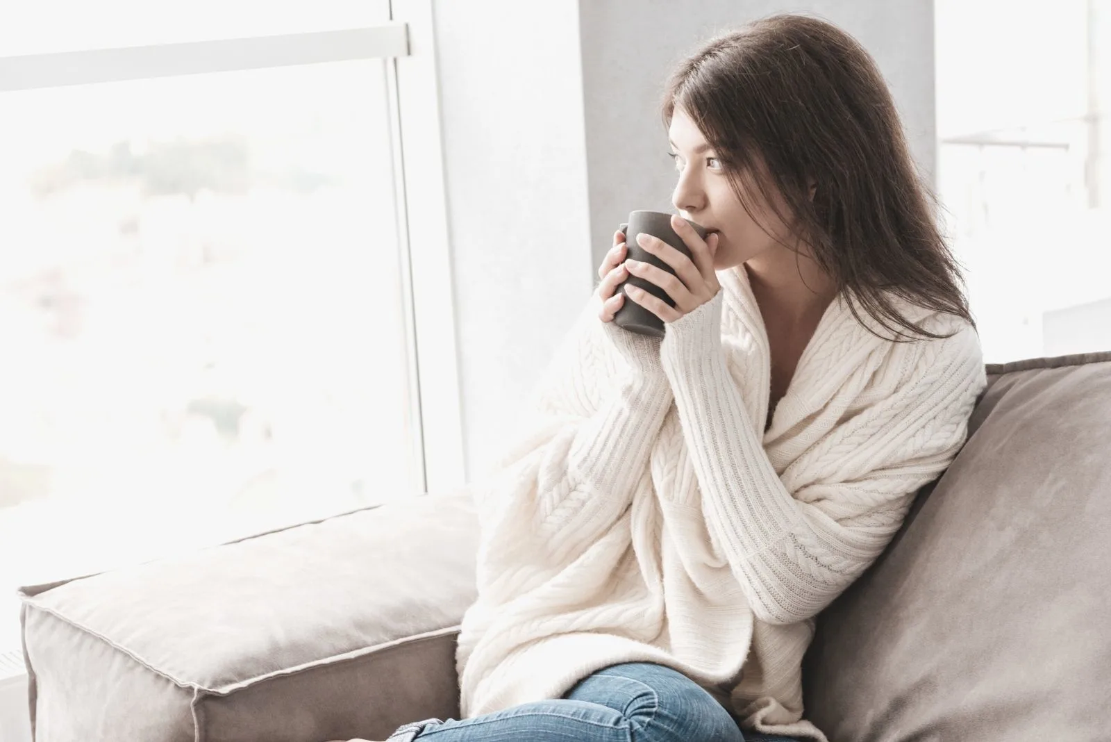 pensive woman drinking from a mug chilling in the sofa inside living room