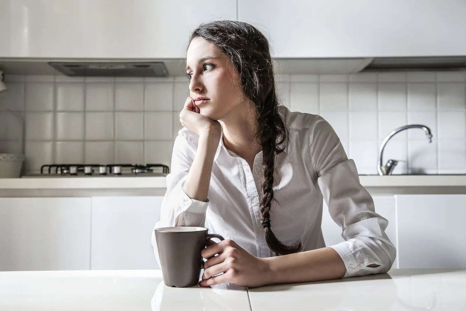 pensive woman drinking coffee in the kitchen looking away 