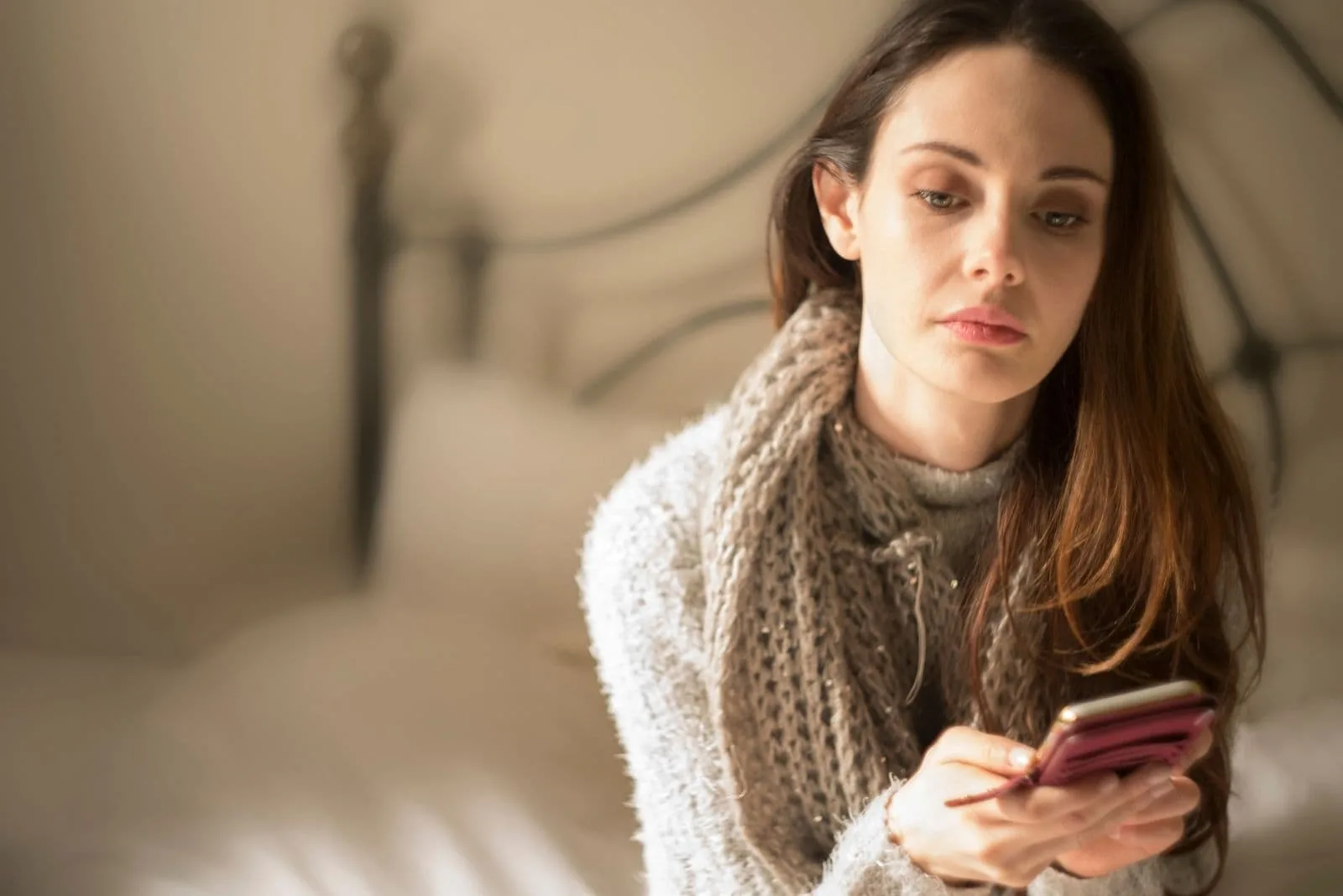 pensive woman in bed holding her smarphone waiting for a reply