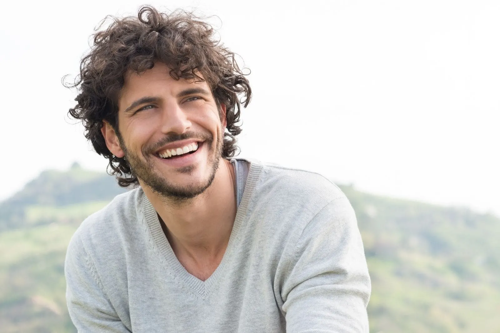 portrait of a happy man with curly hair sitting outdoors and smiling
