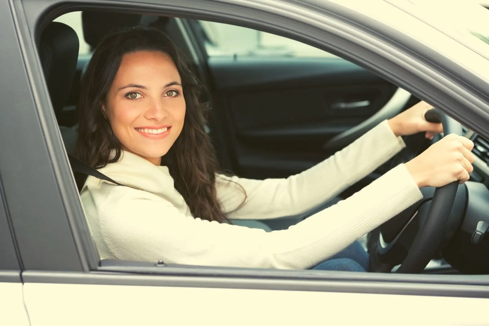 pretty woman driving and smiling to the camera wearing long sleeved shirt