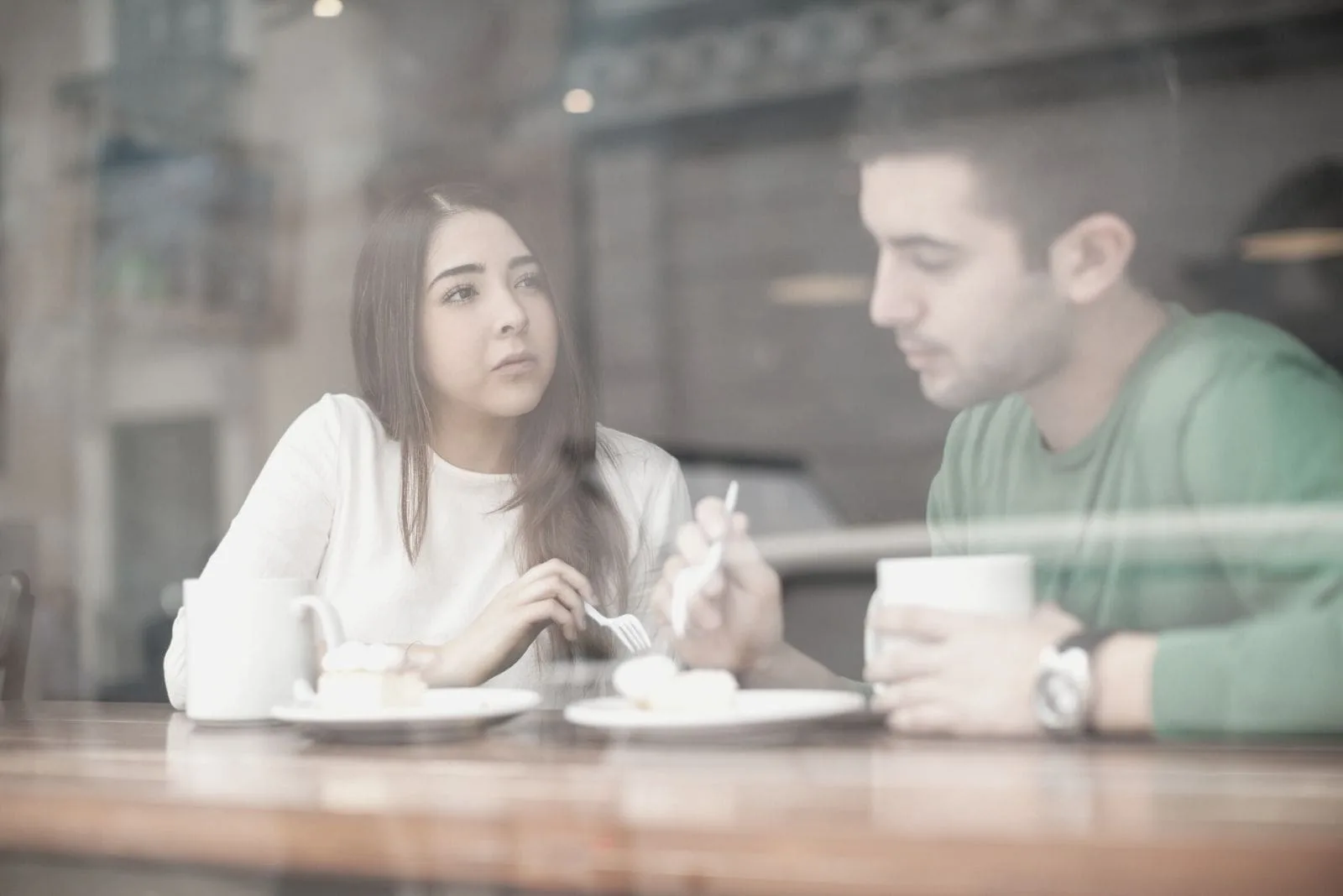 pretty young brunette talking to her boyfriend seriously insde a cafe behind the windows