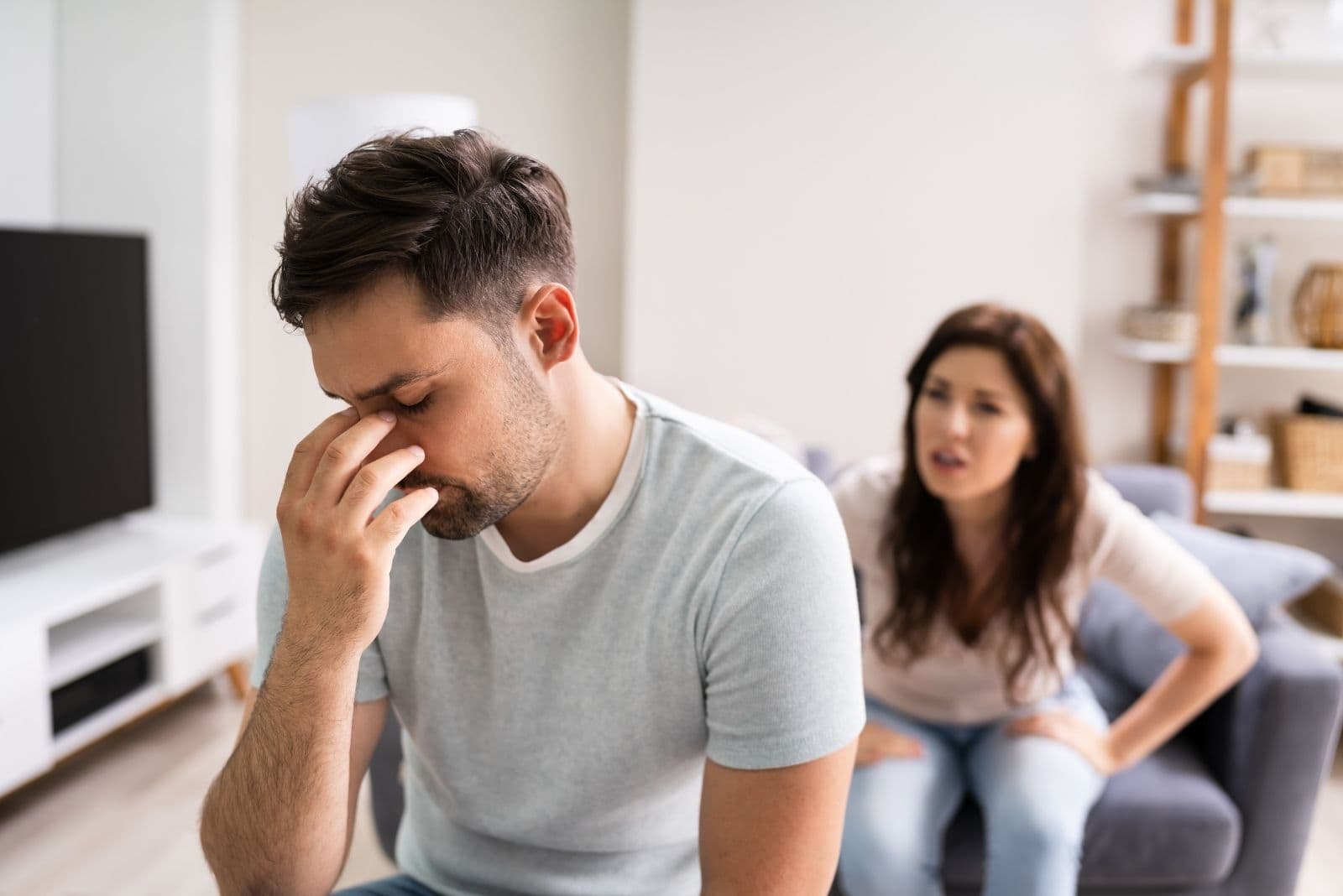 hombre triste con dolor de cabeza mientras su mujer le regaña en el salón