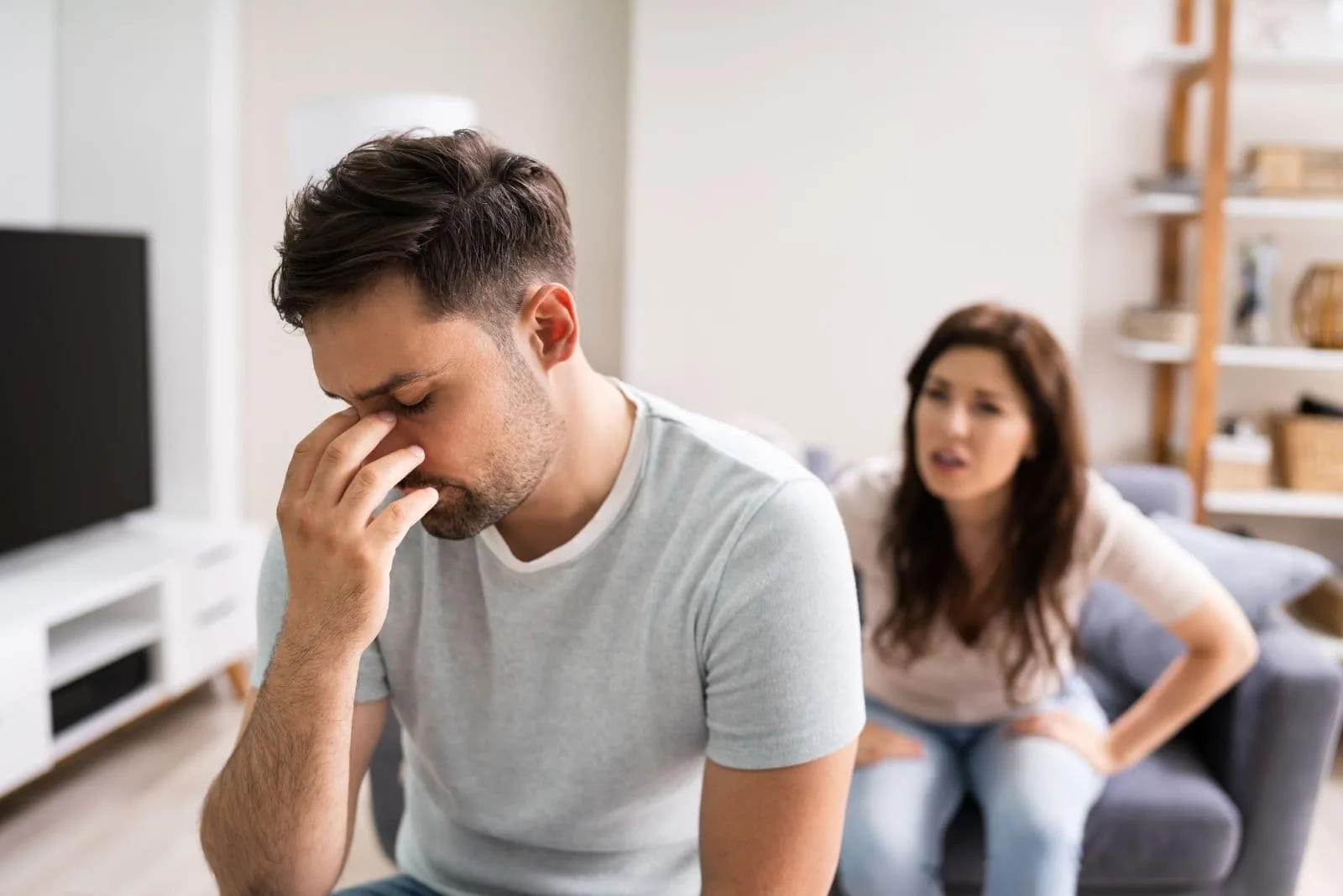 sad man having headache while wife nags him inside living room
