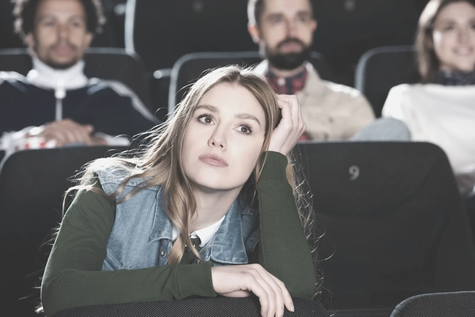 selective focus of a woman watching movie alone with few people at the back inside the cinema