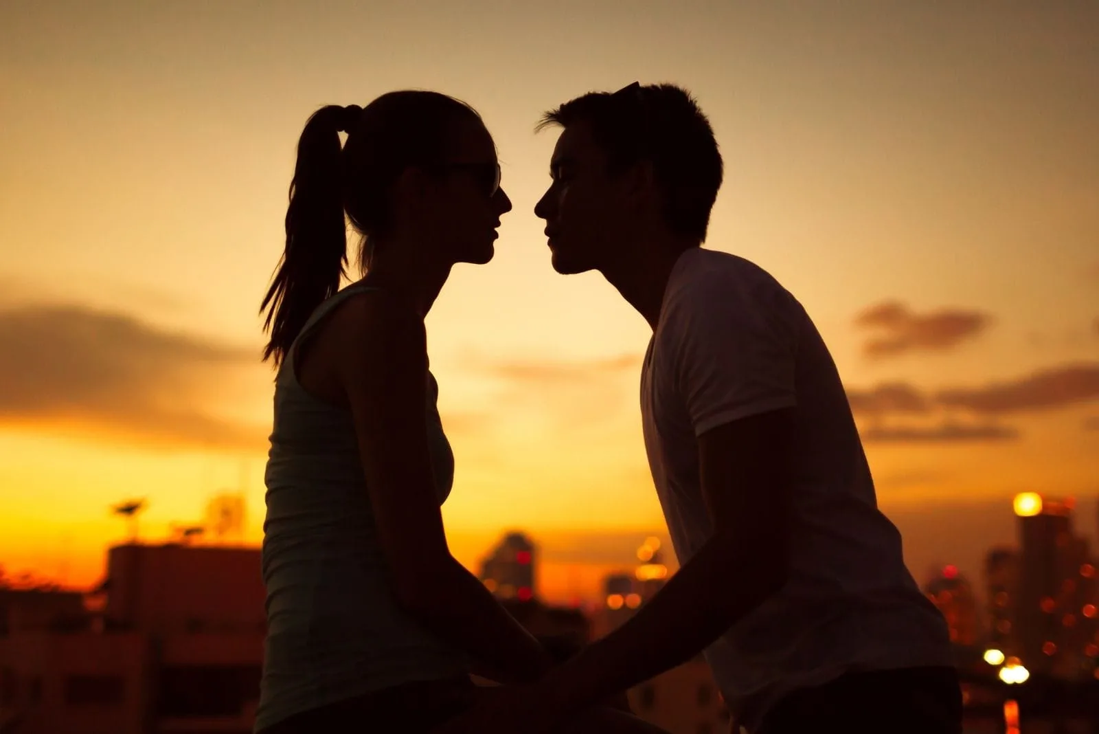 silhouette of a couple kissing while hands holding during sunset