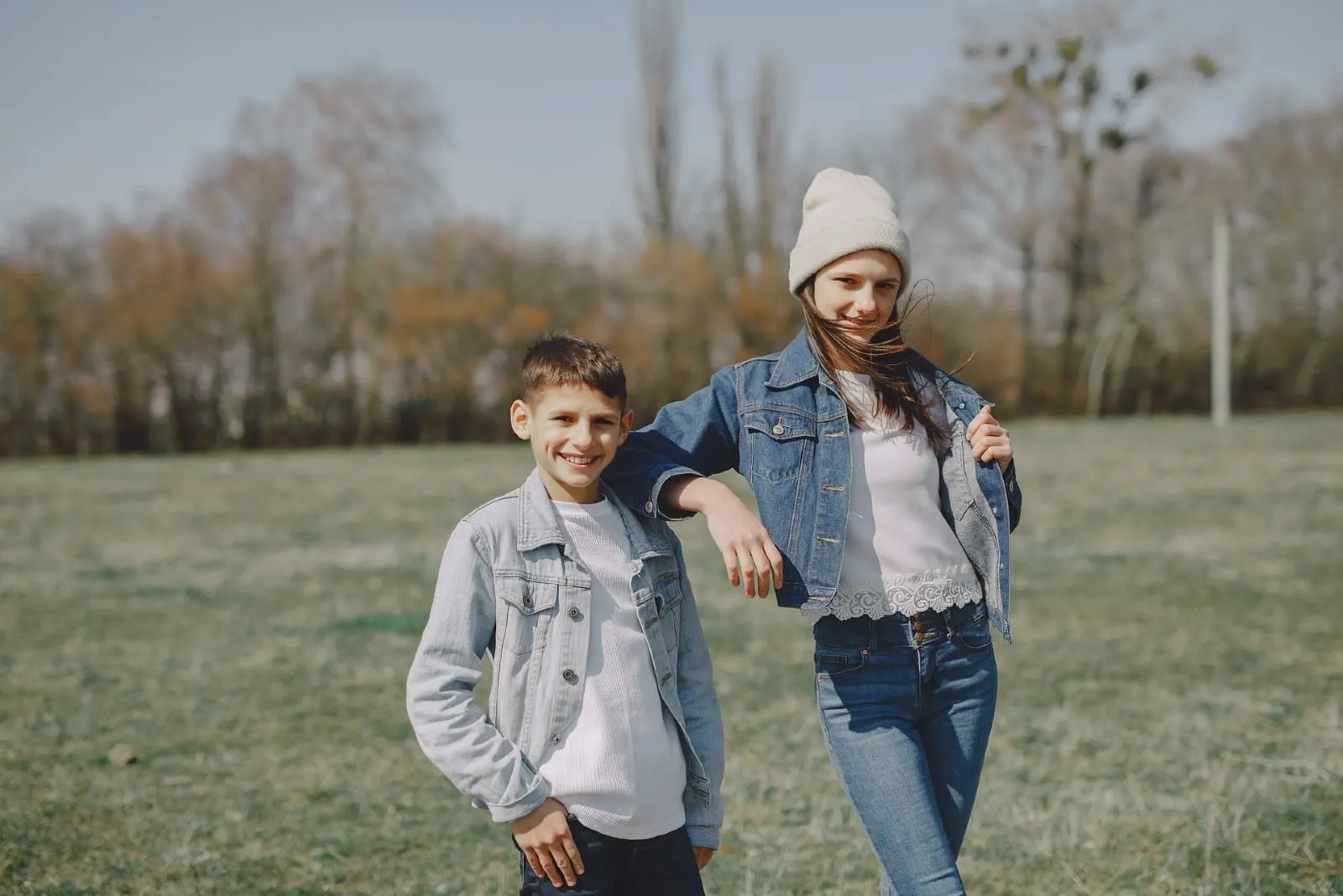 brother and sister in denim jackets standing on grass