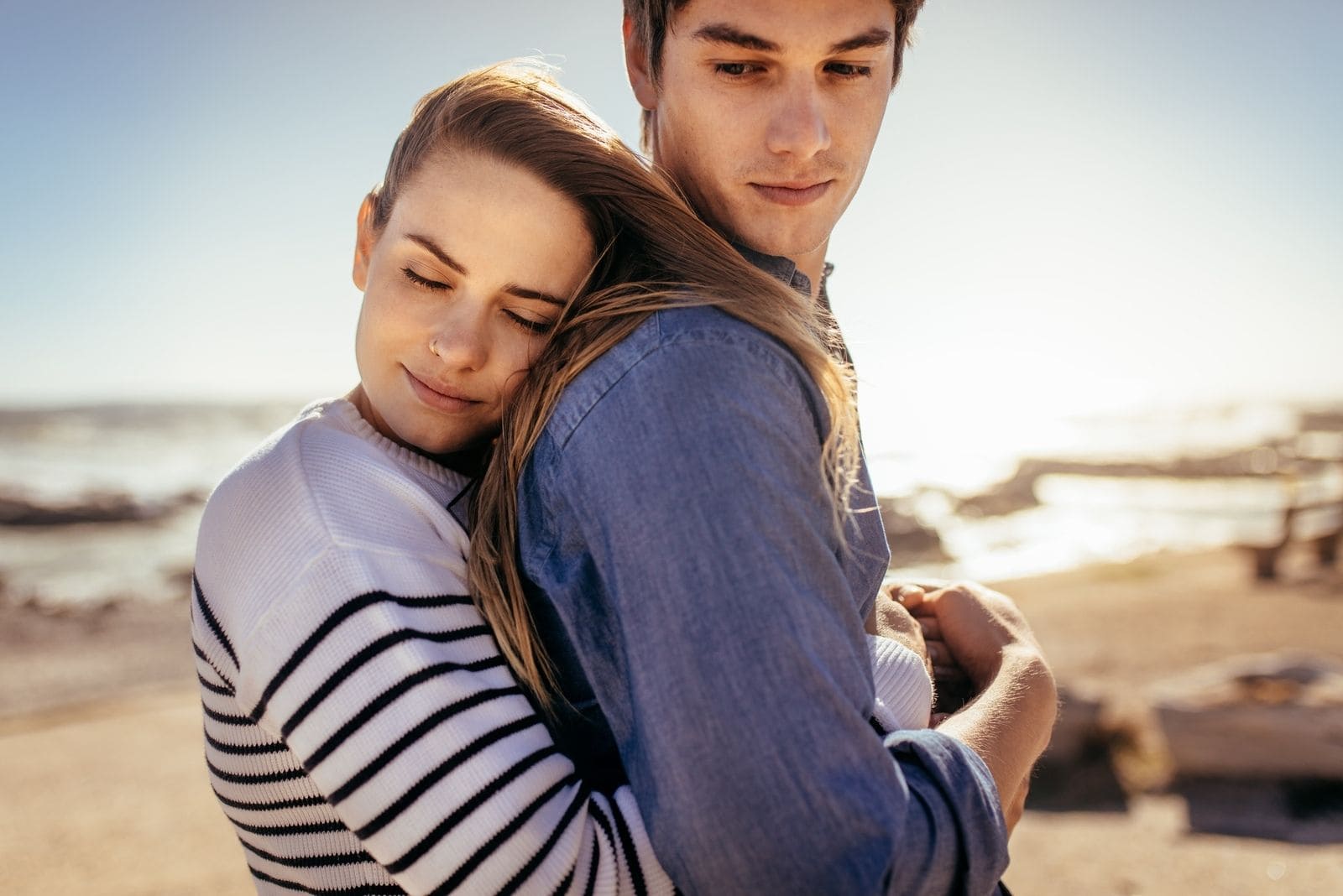 smiling woman hugging her boyfriend from behind standing on the beach