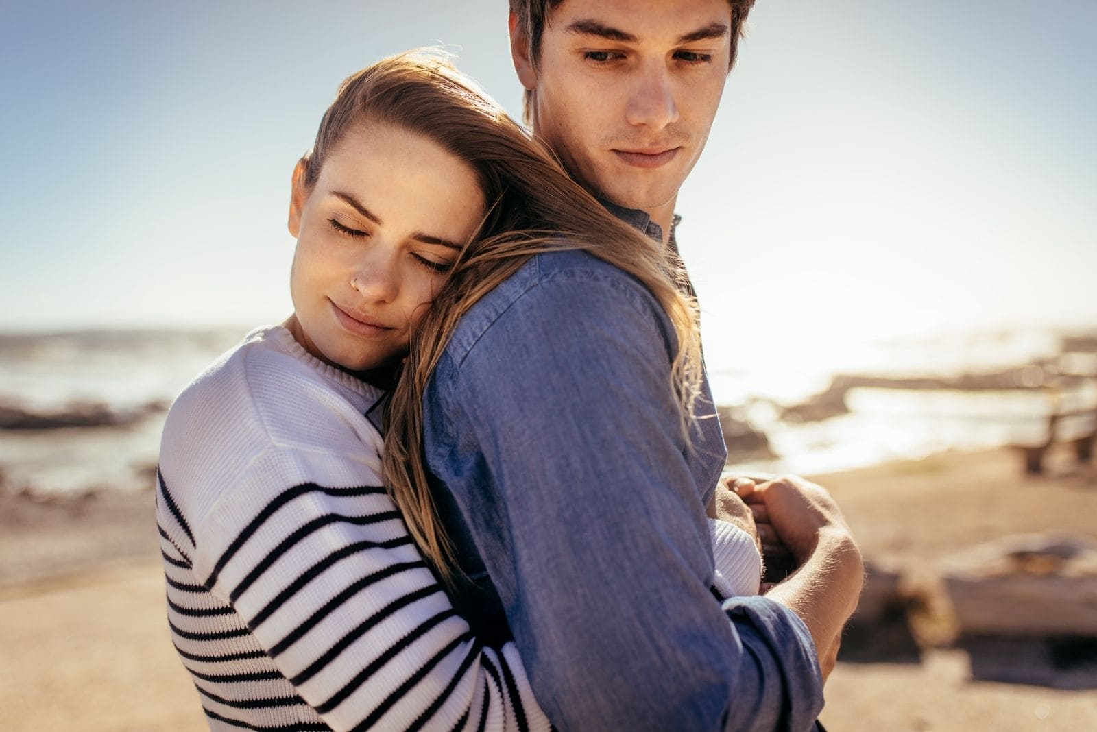 mujer sonriente abrazando a su novio por detrás de pie en la playa