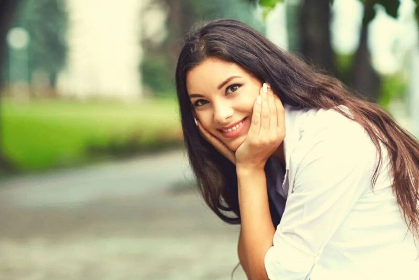 smiling woman sitting at the side of the street with hands supporting her face