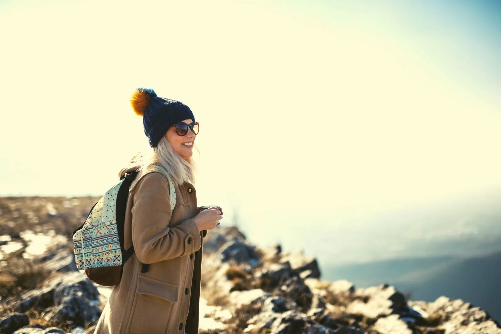 smiling woman standing at the top of the mountain wearing coat and bringing a backpack