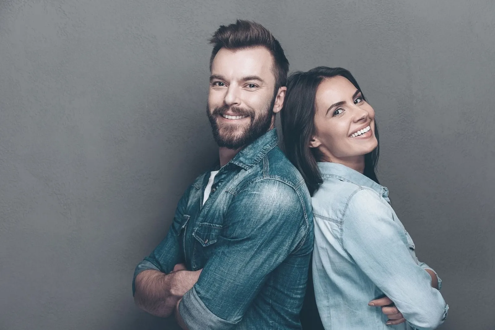 studio shot of a young couple in jeans standing back to back and smiling