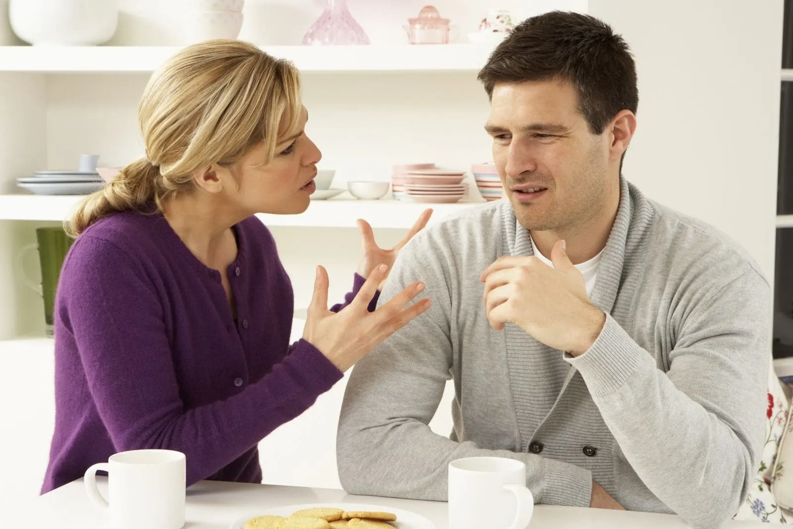 upset woman nagging on man sitting by the table in the kitchen