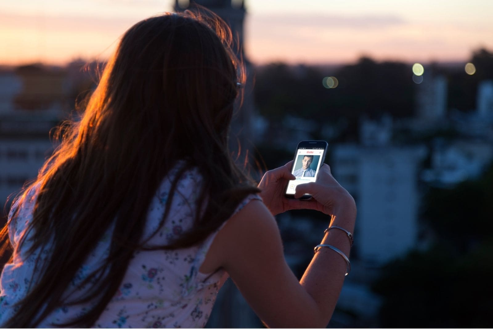 donna al tramonto che fissa il suo smartphone in cima all'edificio