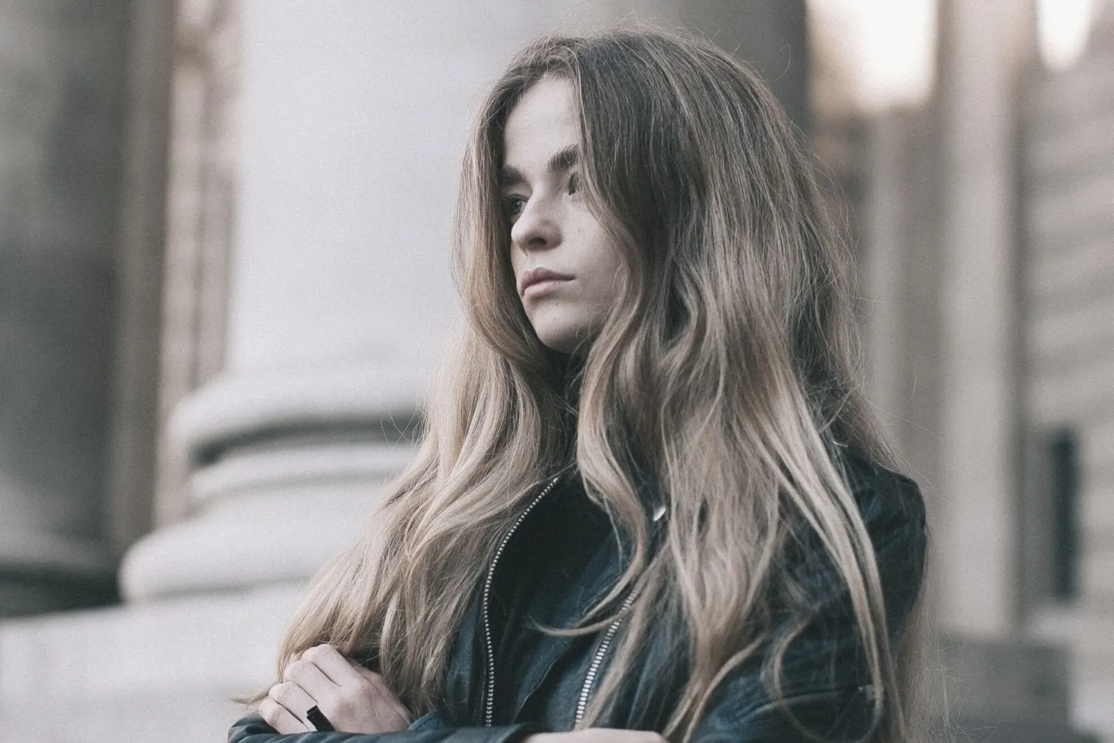 woman black leather jacket standing and thinking deeply outside an old building