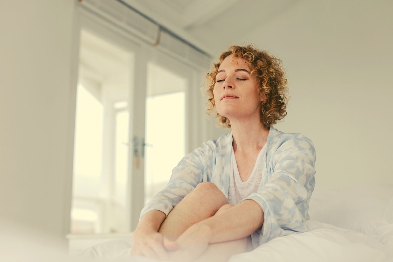 woman closing eyes and sitting in the bed early in the morning