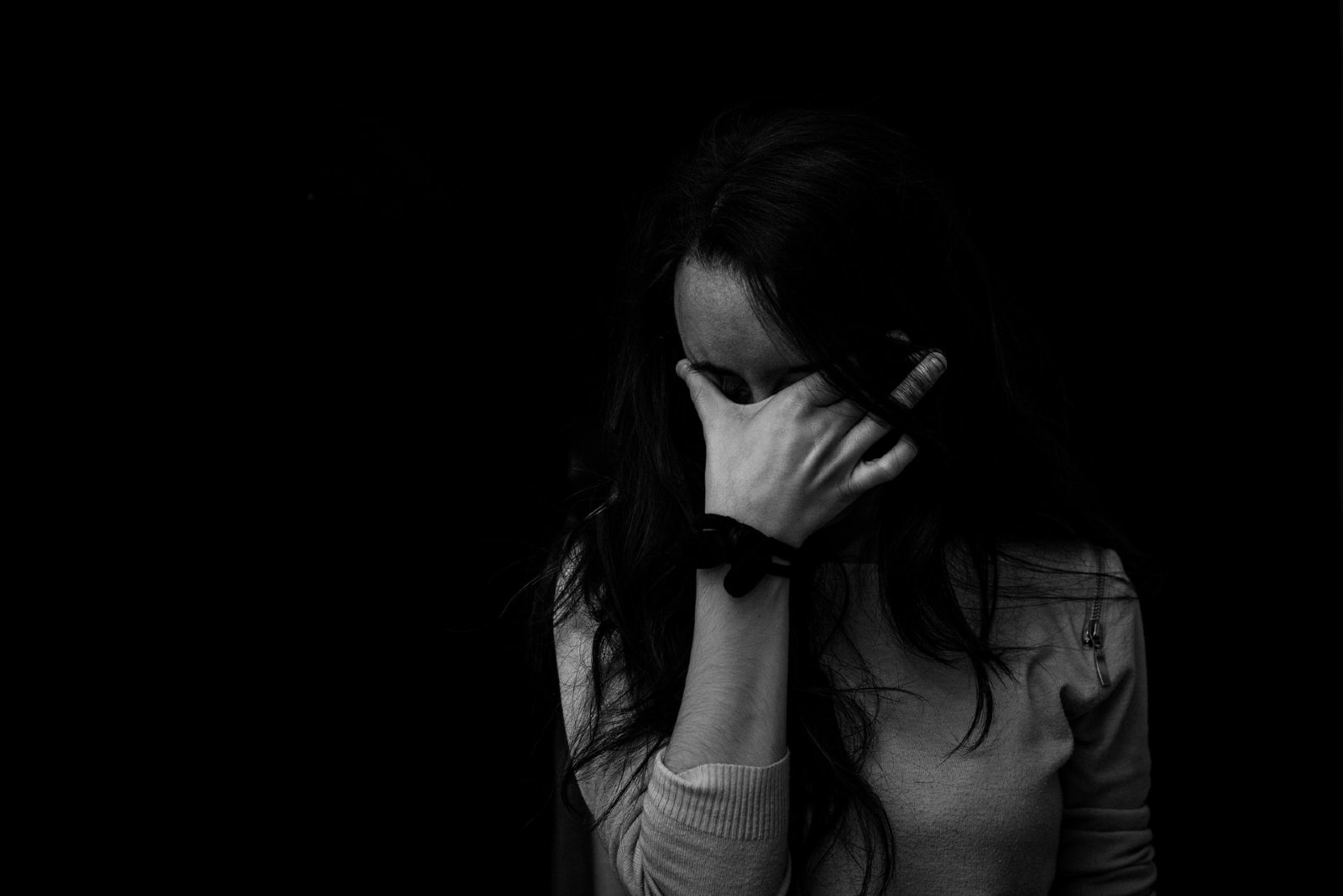 woman covering eyes with hand while standing near wall