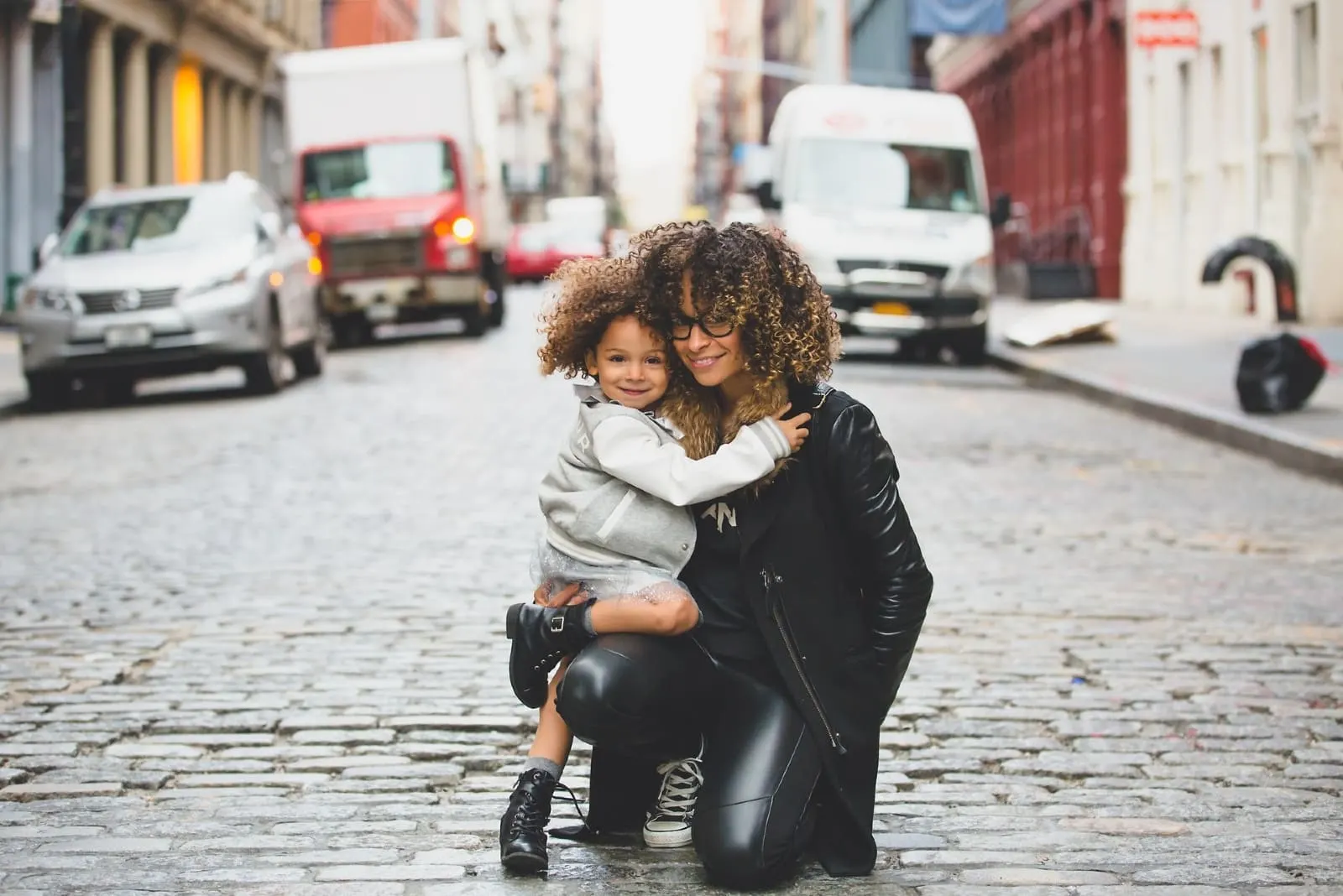 woman with curly hair holding girl on the street