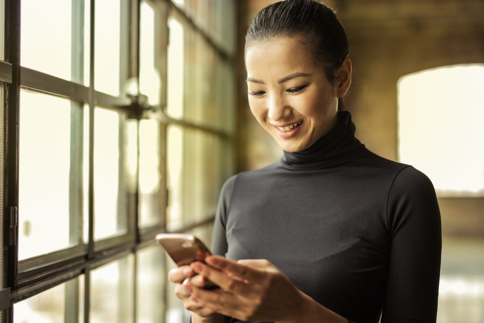 mujer feliz con cuello alto negro sosteniendo un smartphone